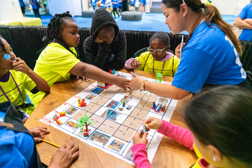 A group of elementary age boys and girls play a board game.